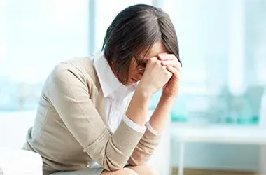Chiropractic Tustin CA headache Person seated with head down and hands on face, indicating headache or stress.
